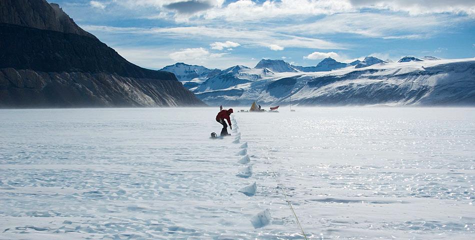 Teammitglied Daniel Baggenstoss nimmt Proben aus dem Eis. Im Hintergrund steht das Forschungscamp. © Hinrich Schaefer